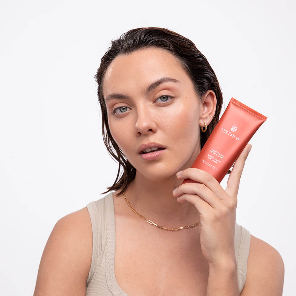 Woman smiling while holding USTAWI Detox Clay Mask Skincare product bottle, showcasing its fresh and rejuvenating packaging