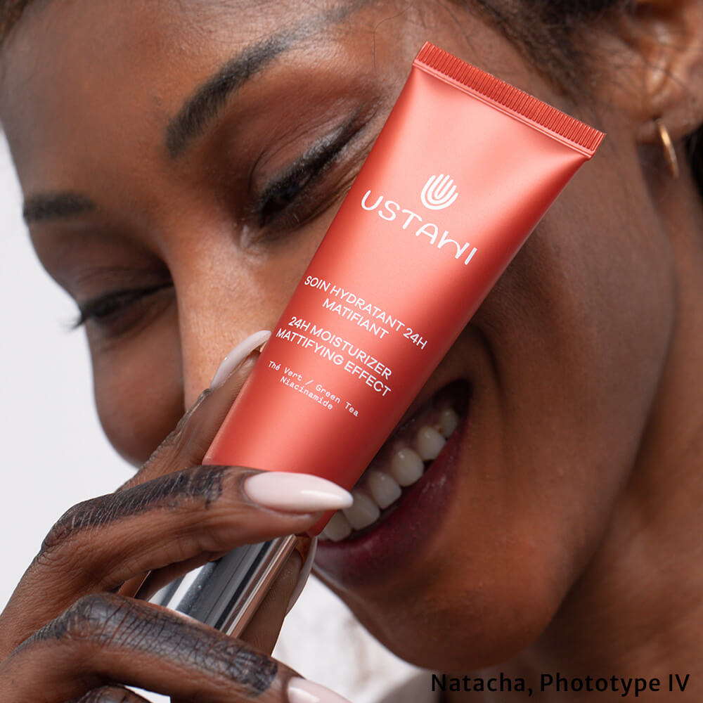 Woman laughing behind a tube of USTAWI 24h Moisturiser Mattifying Effect