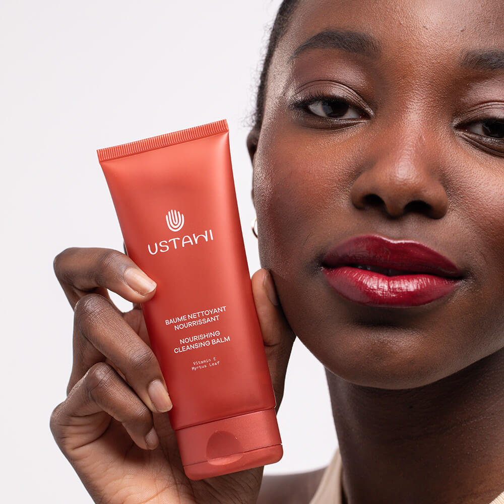 Smiling woman holding a tube of USTAWI natural, nourishing cleansing balm with a gentle texture and soothing ingredients, perfect for all skin types